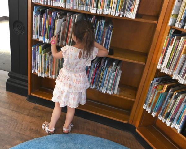 girl looks at books on library shelf